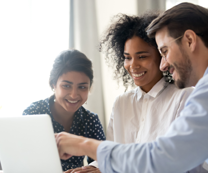 Um homem e duas mulheres sentados em frente a um notebook, olhando para ele e sorrindo.