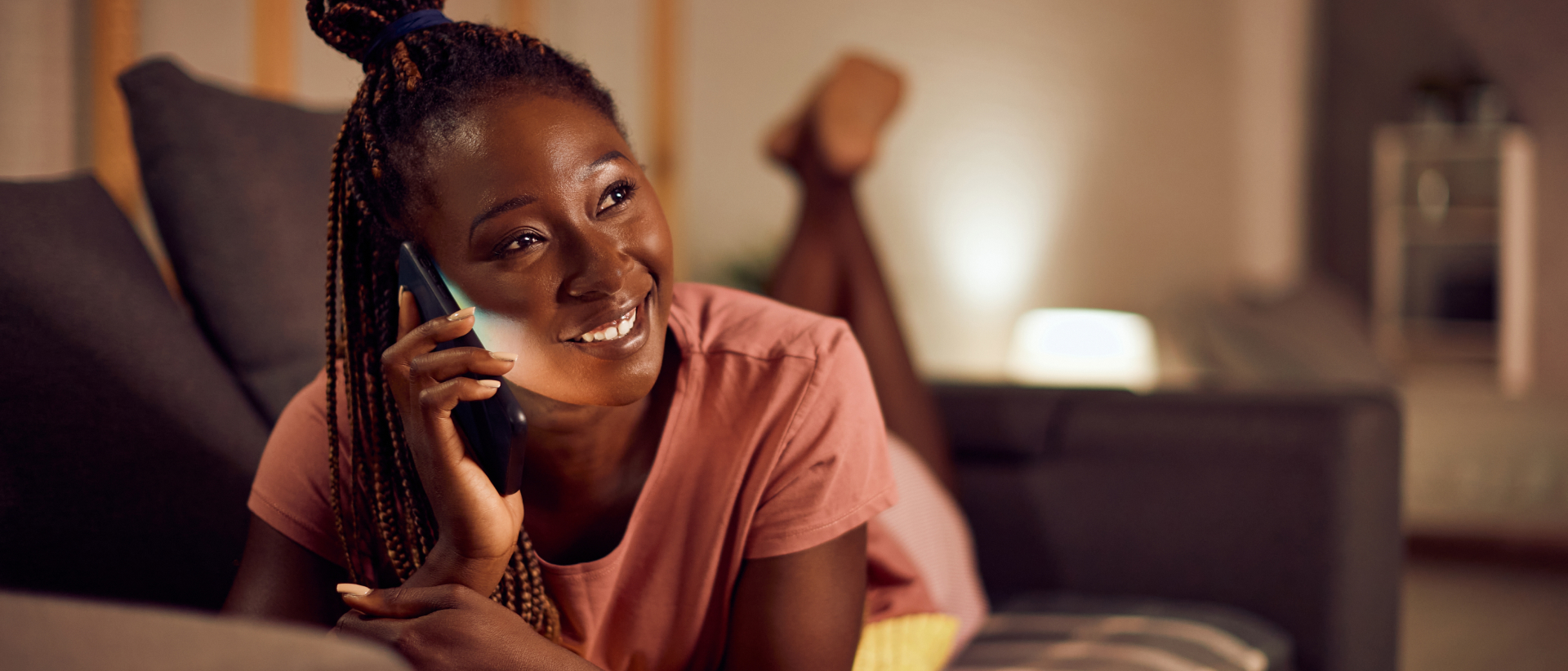 Mulher detada de bruços em um sofá e falando no telefone.