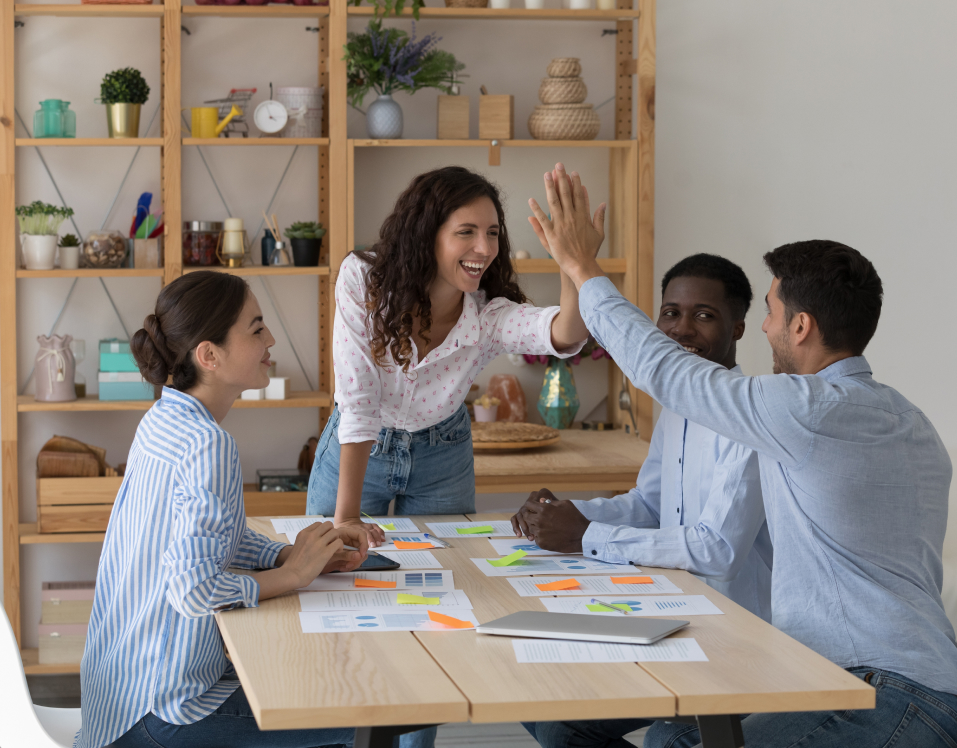 Imagem de quatro pessoas em volta de uma mesa sorrindo e comemorando.